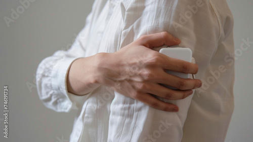 A persons hand holding a compact device that attaches to the back of a shirt and uses gentle electric pulses to stimulate muscles for improved posture.