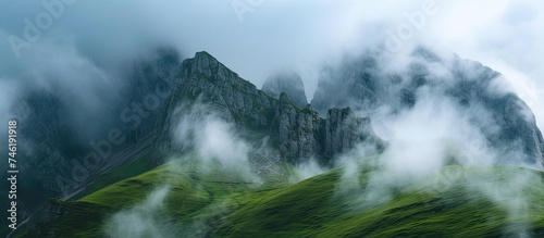 Clouds shroud the peaks of a green mountain in mist, creating a mysterious and atmospheric scene.