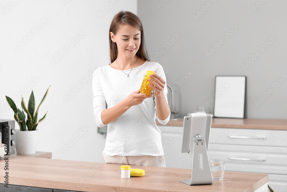 Beautiful woman with bottle of vitamin supplements in kitchen Beautiful woman with bottle of vitamin supplements in kitchen