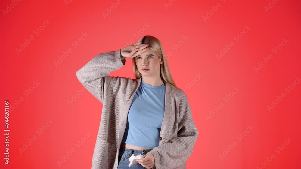 Young woman with fever, blows nose in napkin, isolated red background, studio Young woman with fever, blows nose in napkin, isolated red background, studio