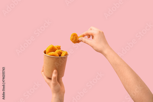 Obraz na płótnie Woman holding paper bucket with tasty nuggets on pink background