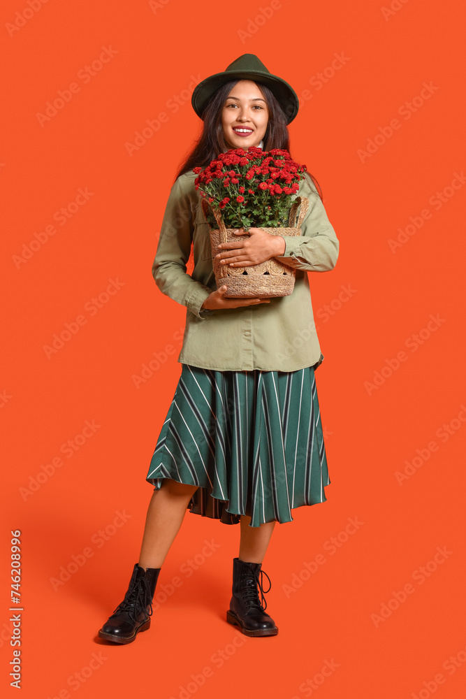Young Asian woman with chrysanthemum flowers on orange background