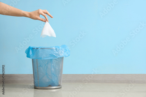 Female hand throwing used tissue into trash bin near blue wall