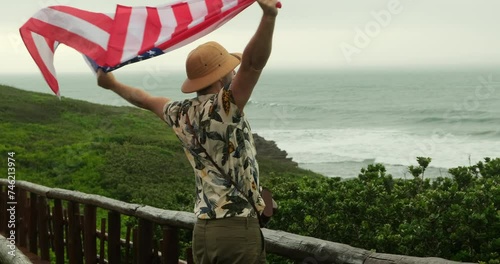 a male traveler holds an American flag proudly. hiker man celebrates u.s. independence day 4th of july on california beach. male solo traveler across america holding an american flag above his head photo