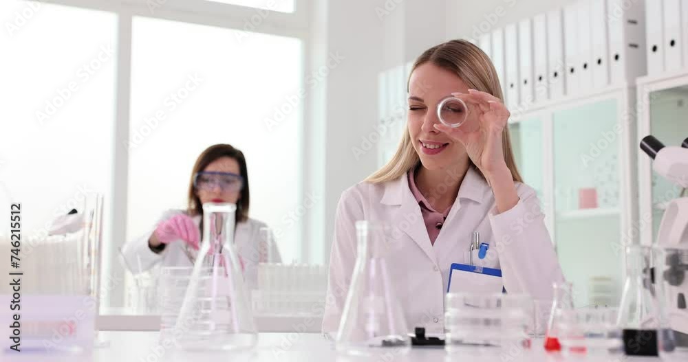 Pretty young biology student in science laboratory smiling through glass flask Pretty young biology student in science laboratory smiling through glass flask