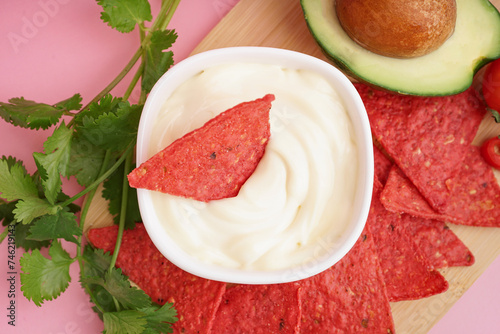 Wooden tray with red nachos, mayo and parsley on pink background