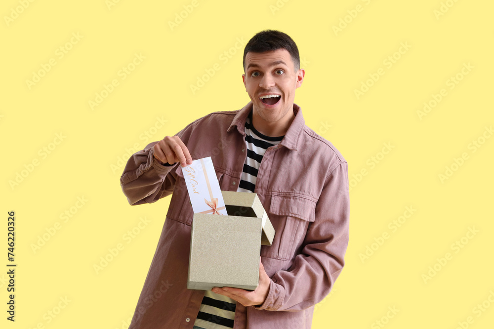 Young man with gift card in box on yellow background Young man with gift card in box on yellow background
