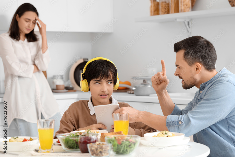 Angry father taking tablet computer away from his teenage son at table during dinner in kitchen. Family problem concept Angry father taking tablet computer away from his teenage son at table during dinner in kitchen. Family problem concept