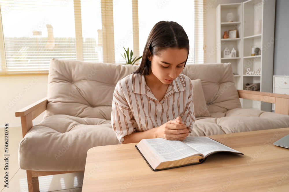 Beautiful young woman reading Bible and praying at home Beautiful young woman reading Bible and praying at home
