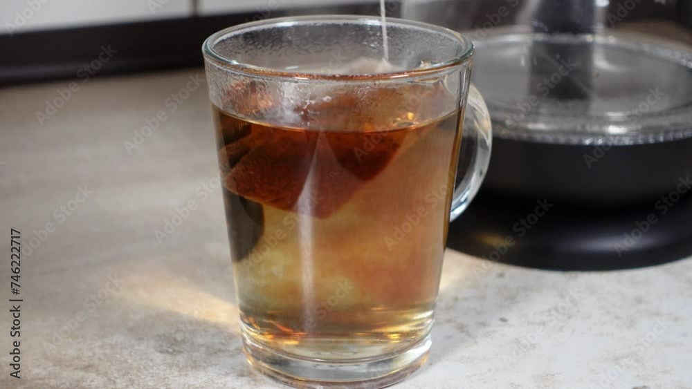 Heisses Wasser wird in ein Glas mit Tee eingefüllt Heisses Wasser wird in ein Glas mit Tee eingefüllt