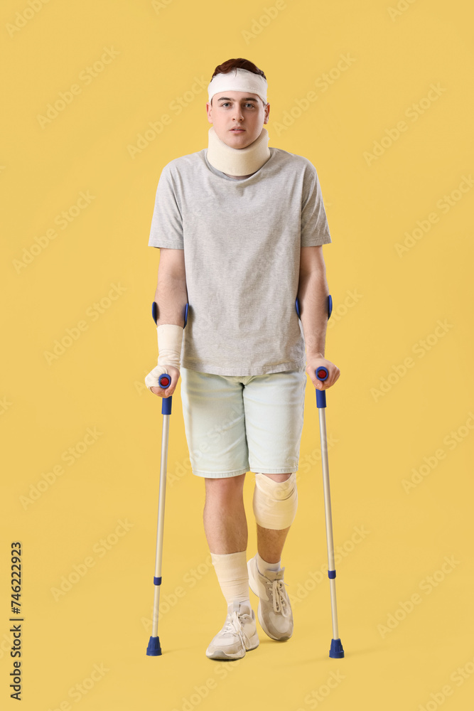 Injured young man after accident with crutches on yellow background Injured young man after accident with crutches on yellow background