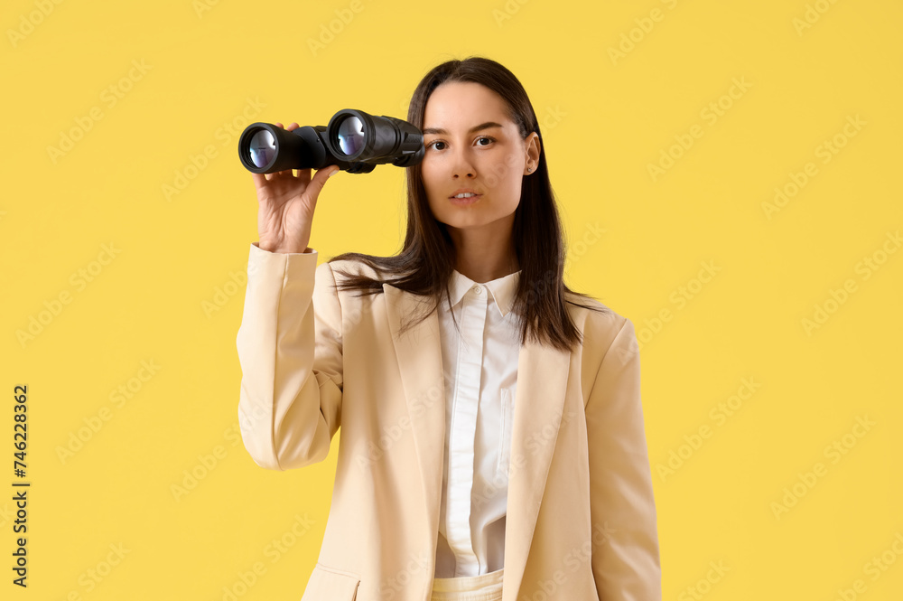 Obraz premium Young businesswoman with binoculars on yellow background