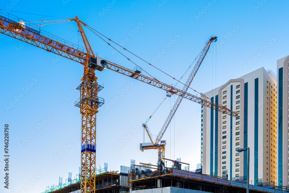 Construction site with cranes, workers and modern buildings on sky background.