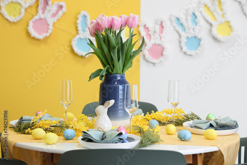 Festive table setting decorated with mimosa flowers  vase of tulips  Easter bunny and painted eggs