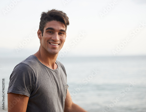 Man, portrait and smile on beach in outdoors, nature and travel on summer holiday in Brazil. Happy male person, relax and peaceful wave on ocean adventure, mockup space and horizon or sky on vacation