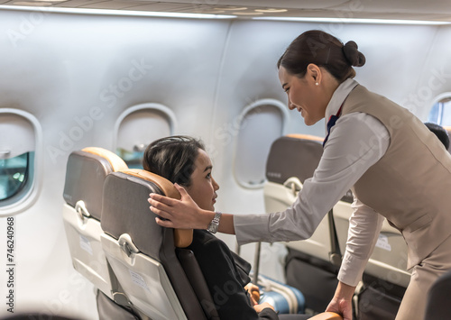 Friendly female airline flight attendant adjust seat for passenger on plane