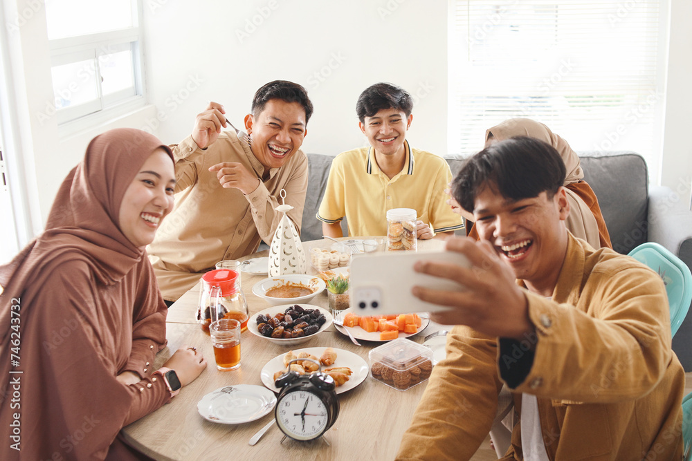 Young muslim friends taking selfie or video call during eating together. Iftar ramadhan and eid mubarak celebration