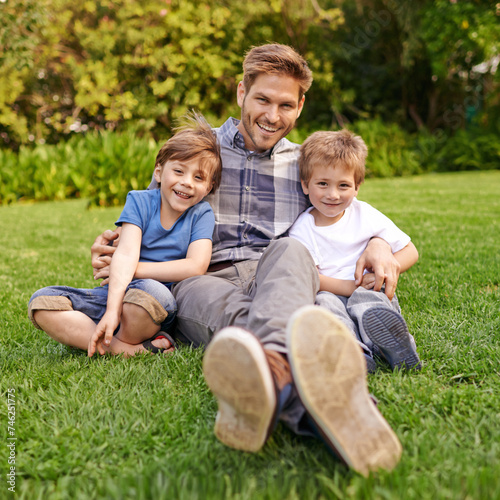 Smile, nature and portrait of children with father relaxing on grass in outdoor park or garden. Happy, family and excited cute boy kids sitting on lawn with young dad for bonding in field together.