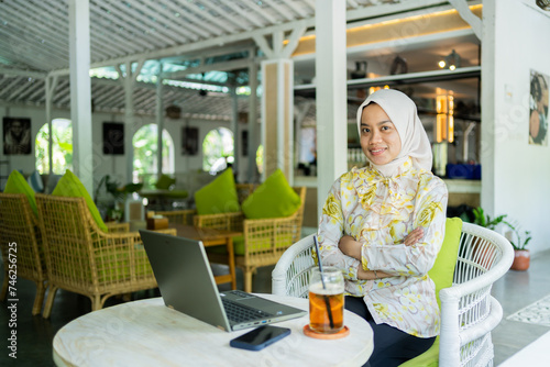 young businesswoman wearing a hijab. Sitting with a smiling face in a cafe, working anywhere.