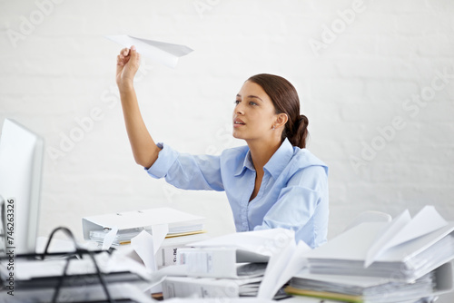 Corporate, businesswoman and paper plane at desk, sitting and thinking while working. Employee and paperwork with files in professional workspace, procrastination and avoid with distraction game photo