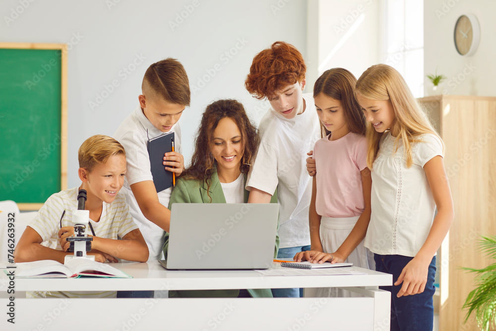 Teacher provides assistance to a group of students at school classroom. With a laptop, the teacher engages in the educational journey alongside pupils, conveying teacher and children teamwork .