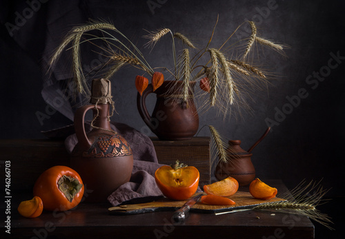 Autumn still life with persimmons and rye in a clay jug on a dark background