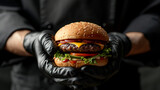 A cook's hands, clad in sleek black gloves, carefully present a mouthwatering cheeseburger against a striking black backdrop, emphasizing its delectable appeal and culinary expertise.