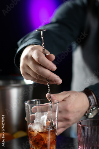 Bartender mixing perfect cocktail with long stirring metal spoon