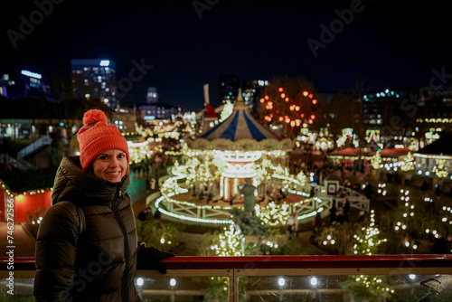 Christmas amusement park. The woman smiles and looks at the glowing landmarks.