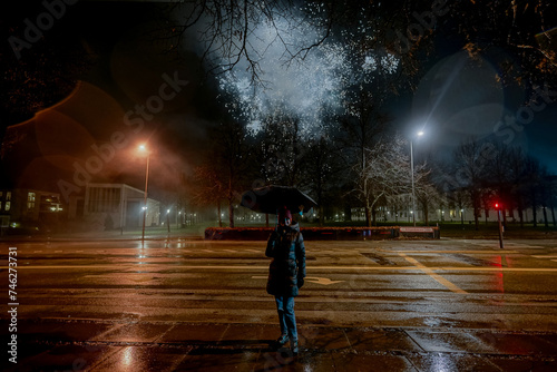 Firework. A girl with an umbrella stands in the middle of the road. Launching fireworks in the background.