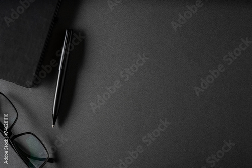 Top view of ballpoint pen, glasses and notepad lying on dark gray table photo