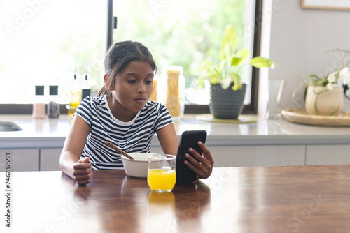 Biracial girl has breakfast at home, focused on her phone photo