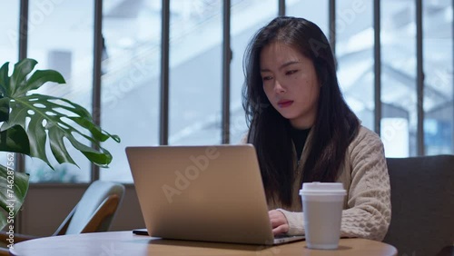 Young Asian girl in bad mood working online on her laptop from cafe., highly disappointed with unsuccesful project. photo