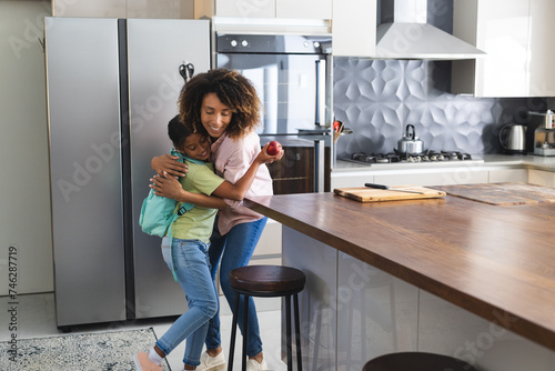 Biracial mother hugs her biracial daughter in a modern kitchen photo