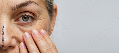 Cropped woman face with fingers under eye with wrinkles showing aging photo