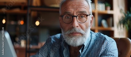 A senior man with a white beard and glasses is sitting in front of a laptop, managing finances and paying bills online. He looks focused and engrossed in his work.