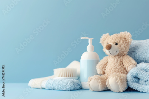 Baby bath accessories, teddy bear sits beside baby lotion, brush, and towels on blue © kheat