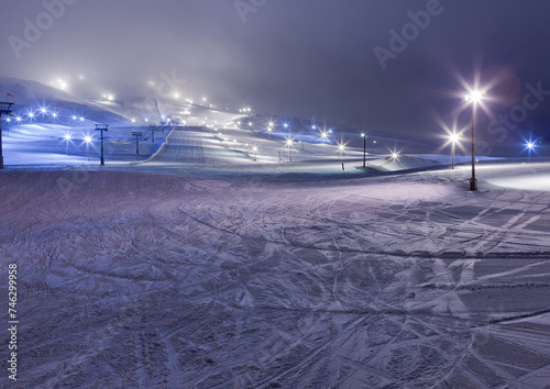 A snowy landscape with lights and ski lift tracks