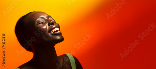 A woman with a radiant smile on her face  her face is brightly lit  in front of an orange background.