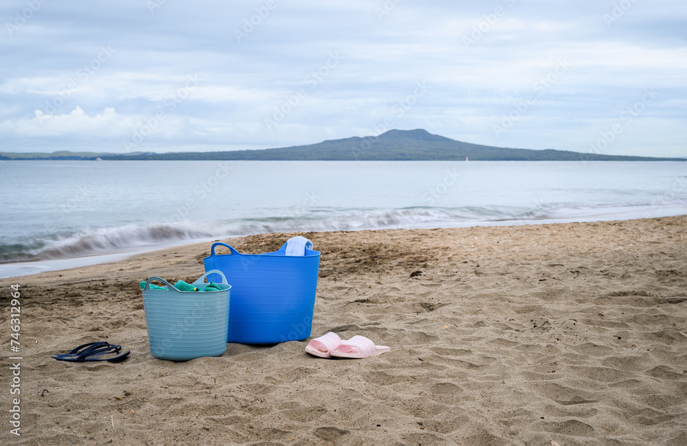 Jandals and buckets on the beach. Rangitoto Island in the distance. Milford Beach. Auckland. Jandals and buckets on the beach. Rangitoto Island in the distance. Milford Beach. Auckland.