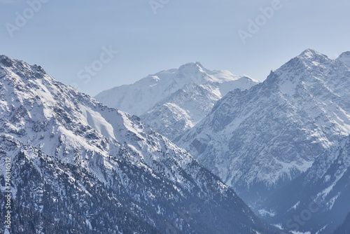 Mountain range, snow capped peaks, border between forest and highlands. Natural scenery background. Karakol gorge landscape. Winter in Kyrgyzstan mountains. Central Asia, Kirgiziya, recreation area