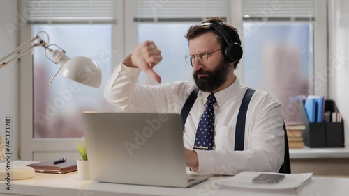 Businessman NO gesture. Disgruntled executive in headphones on video call showing disagreement in remote meeting. Office worker refusing at internet conference photo