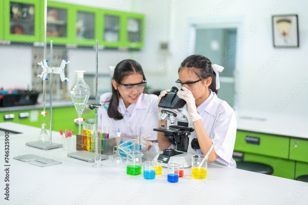 Two Asian female scientists Test chemicals in a biological laboratory in the Ministry of Science. On the table are equipment such as pipers, microscopes, and medical vaccine production. Two Asian female scientists Test chemicals in a biological laboratory in the Ministry of Science. On the table are equipment such as pipers, microscopes, and medical vaccine production.