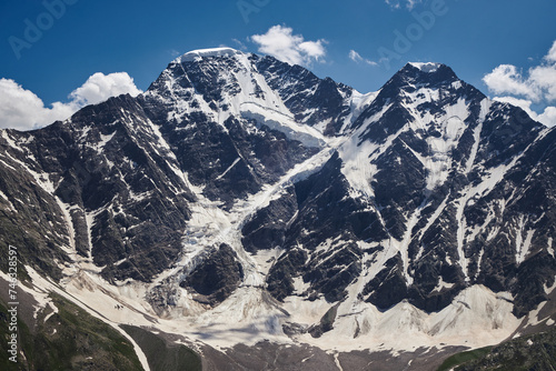 Majestic snow-capped mountains with deep crevasses and glaciers against a blue sky with wispy clouds