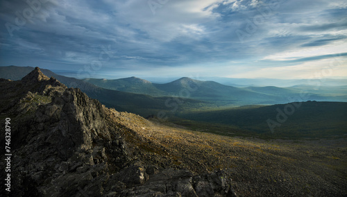 Rugged mountain ridge under a dramatic sky casts shadows over the vast, serene landscape stretching into the distance. Panoramic Landscape © angel_nt