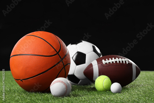 Many different sports balls on green grass against black background