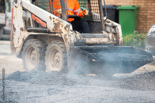 Asphalt paver filled with hot tarmac laying new road surface on new residential housing development site and roadworker operator in orange hi-viz next to it photo