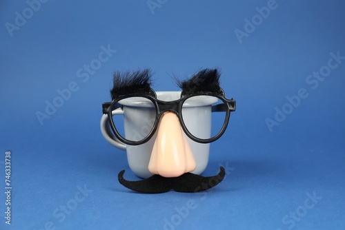Man's face made of cup, fake mustache, nose and glasses on blue background