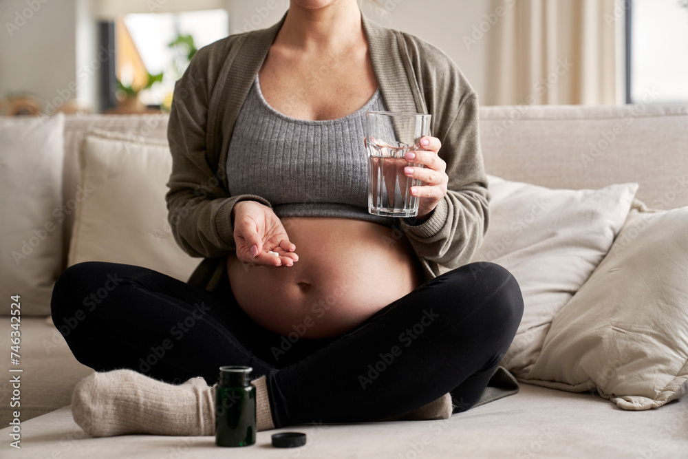 Caucasian pregnant woman sitting on sofa and taking nutritional supplements