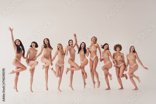 No filter studio photo of shiny charming women wear lingerie enjoying women rights jumping isolated beige color wall background